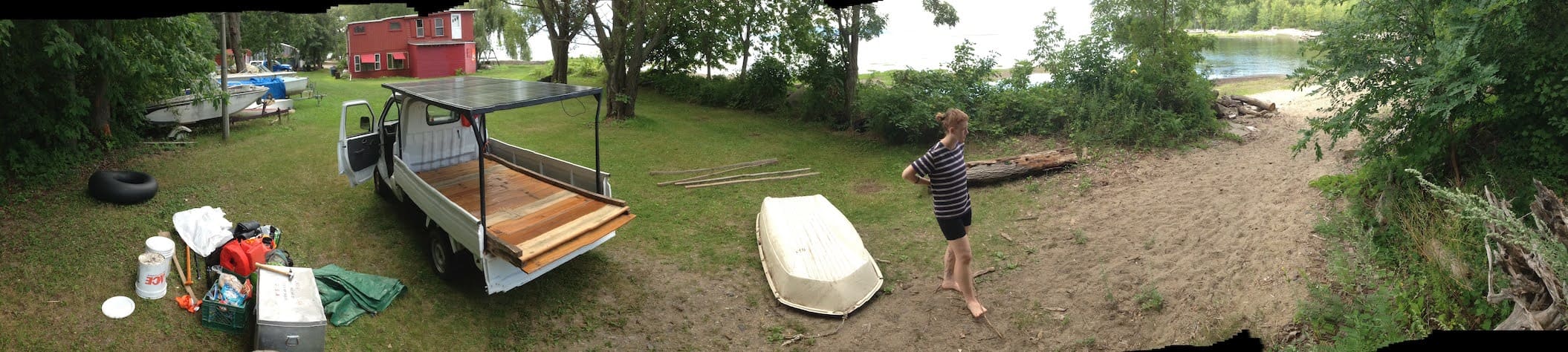 panorama of the solar pickup truck, an overturned boat, a red haired woman and the beach off to the right