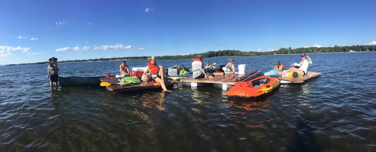 eight people on boats and rafts in a lake with blue sky