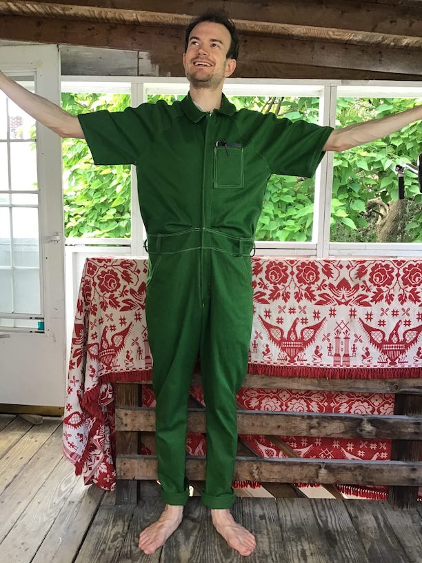 white man wearing green jumpsuit with arms in the air smiling